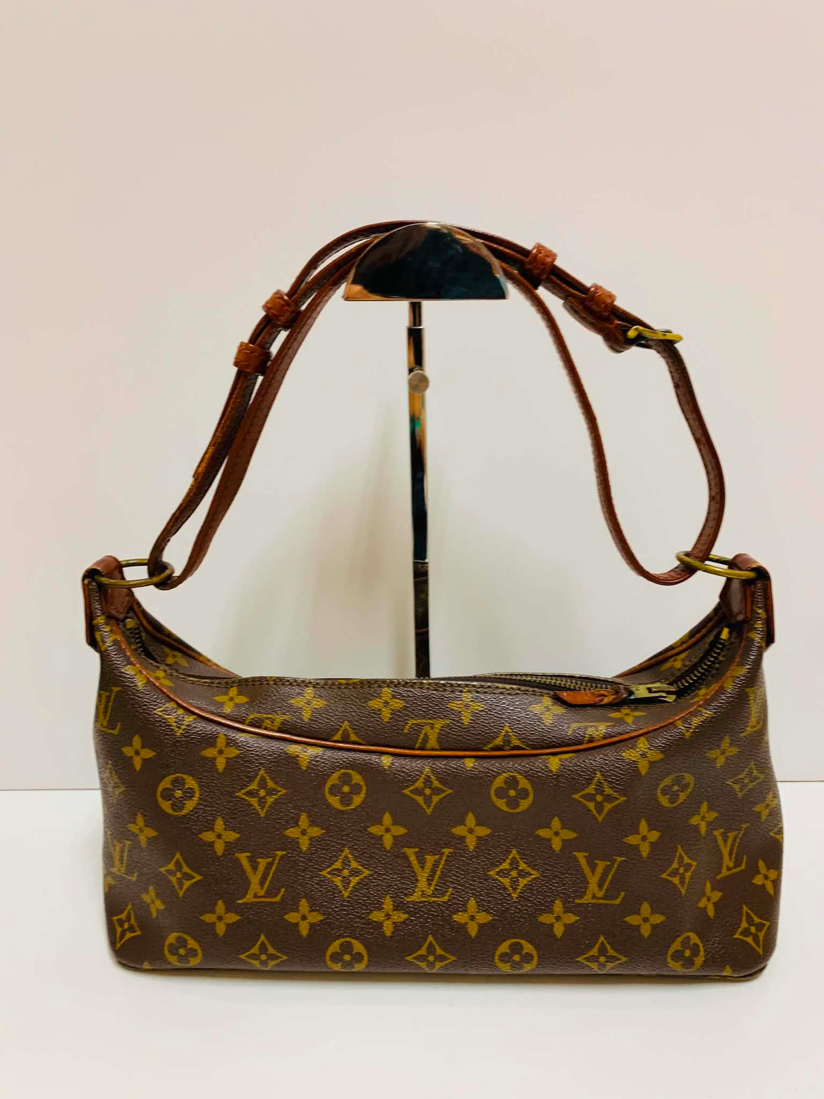 A Louis Vuitton monogram shoulder bag in brown coated canvas with gold-tone hardware, displayed on a black stand against a plain off-white background.
