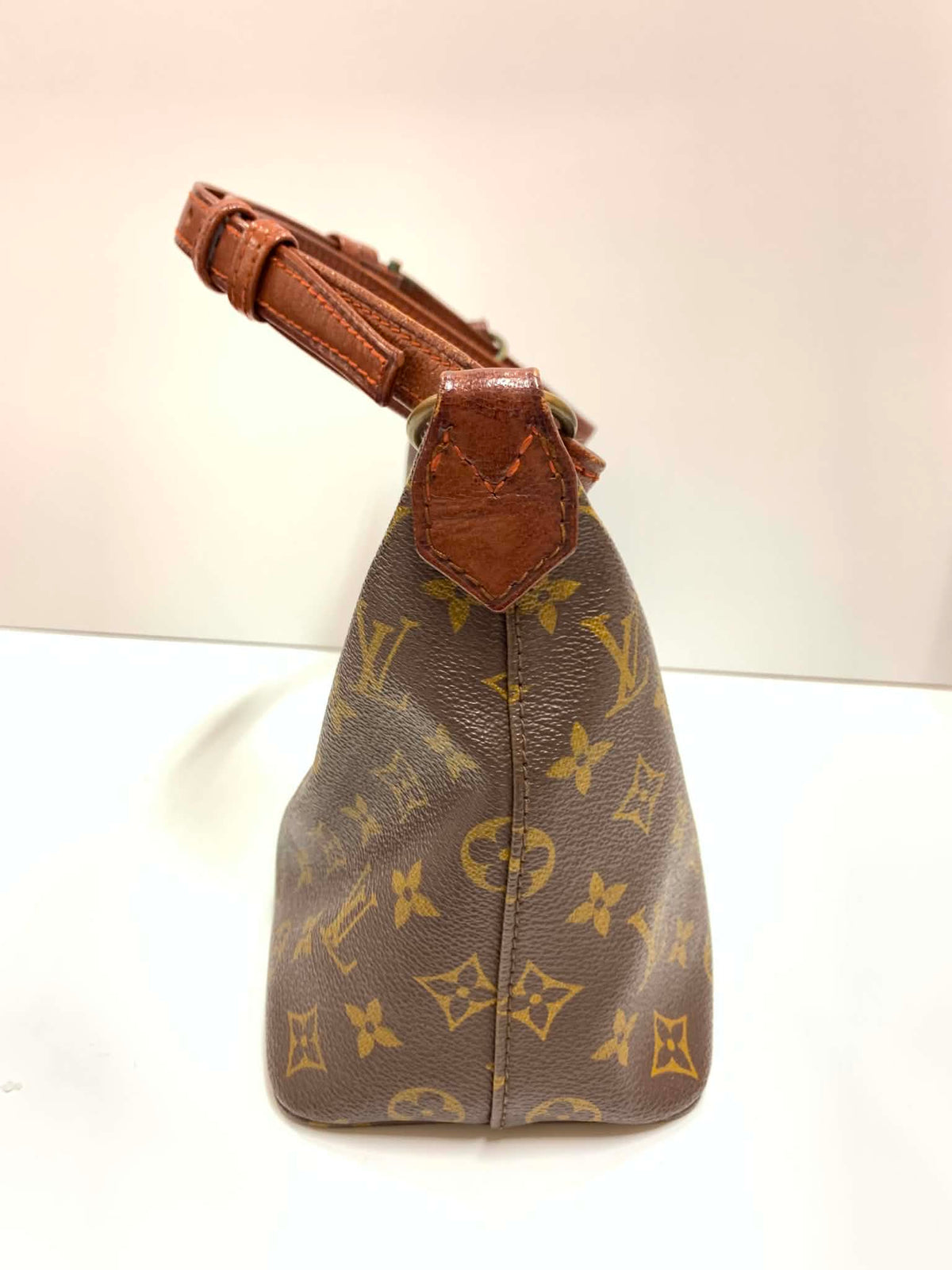 A Louis Vuitton monogram canvas handbag with brown leather trim and a brown shoulder strap, shown from a side angle on a plain light background.