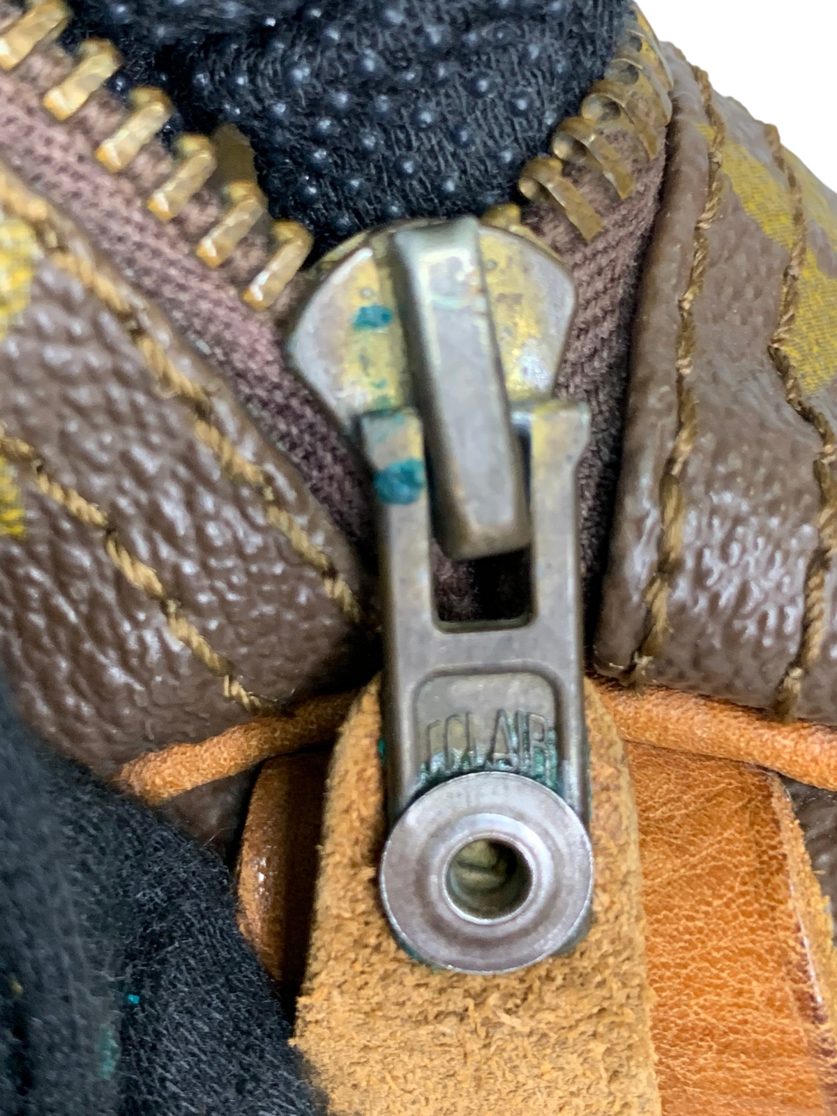 Close-up of a vintage metal zipper pull on a brown monogram canvas travel duffel bag with leather trim.