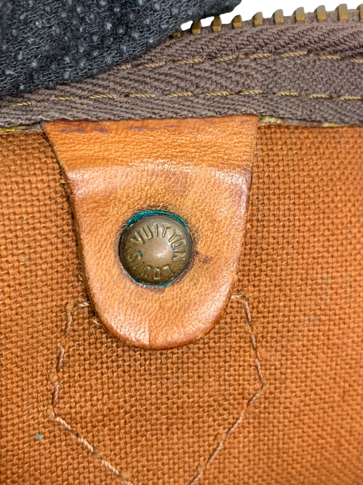 Close-up of a Louis Vuitton monogram canvas duffel bag showing a leather tab with a branded brass rivet.