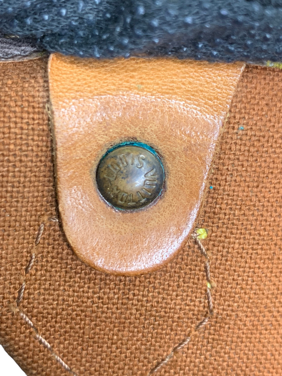 Louis Vuitton monogram canvas duffel bag detail showing a branded brass rivet on tan leather trim.