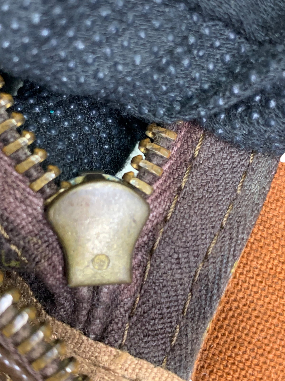 Close-up of a brass metal zipper pull on a brown monogram canvas travel duffel bag with dark fabric lining.
