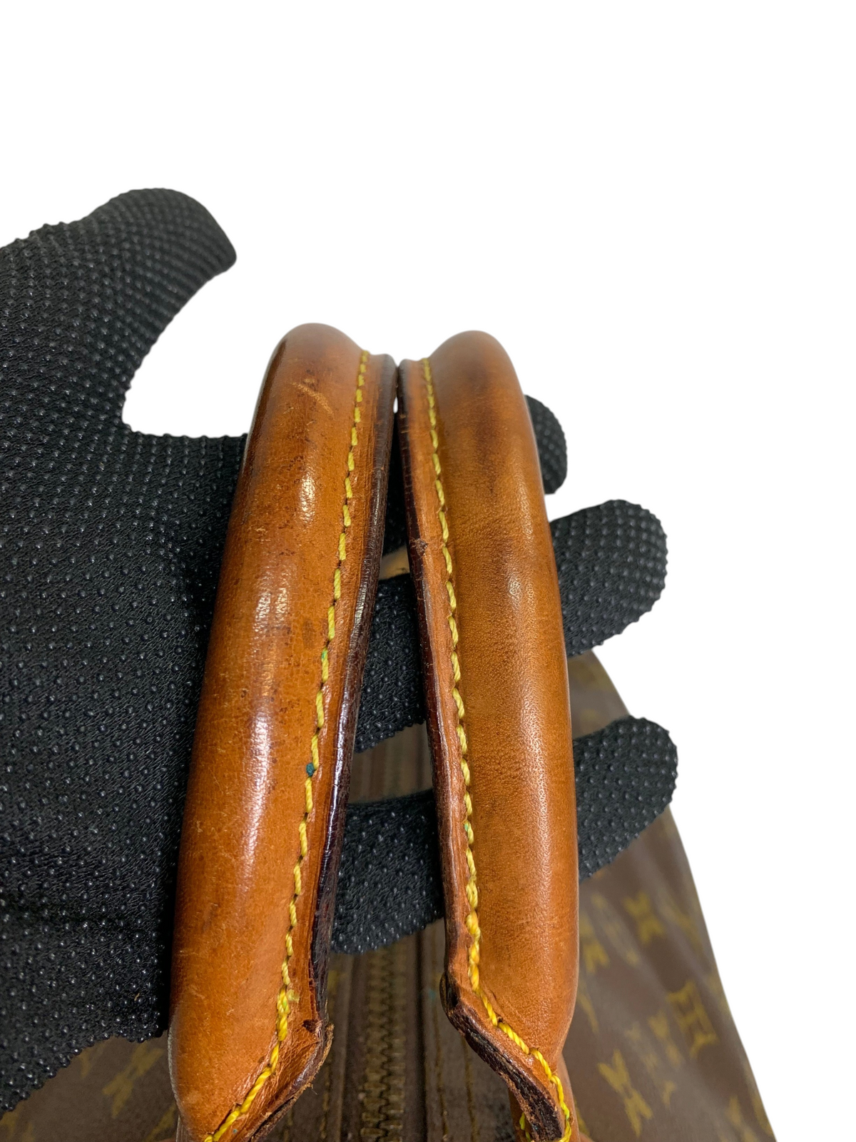 Close-up of brown leather rolled handles with yellow stitching on a monogram canvas travel duffel bag.