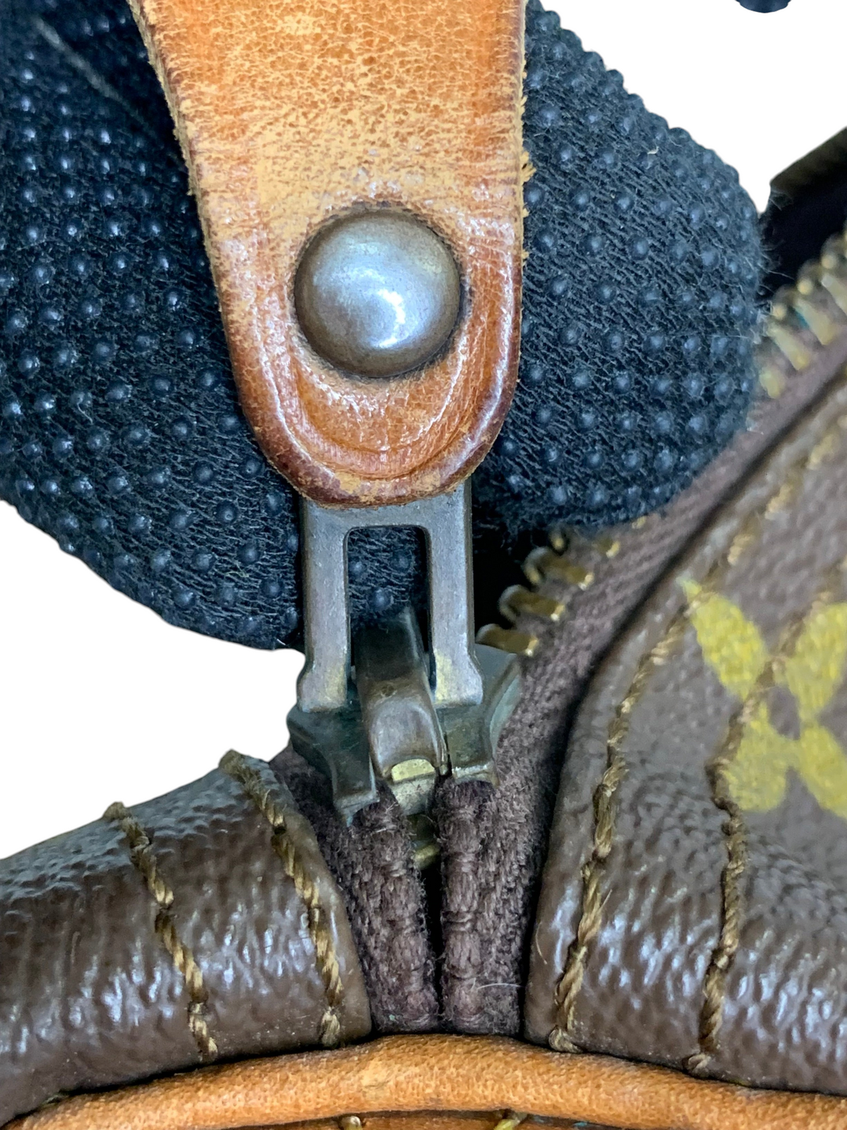 Close-up of a monogram canvas duffel bag zipper pull with worn leather trim and metallic hardware details.