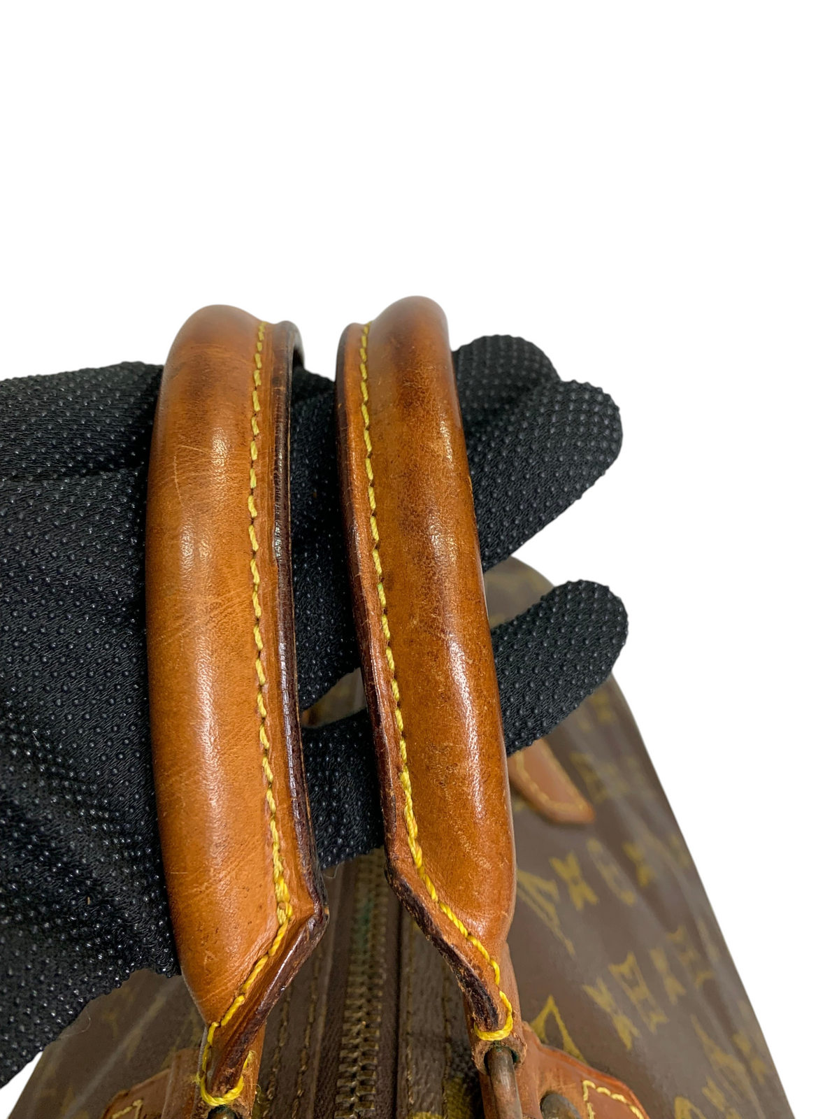 Close-up of brown leather rolled handles on a monogram canvas travel duffel bag with yellow contrast stitching.