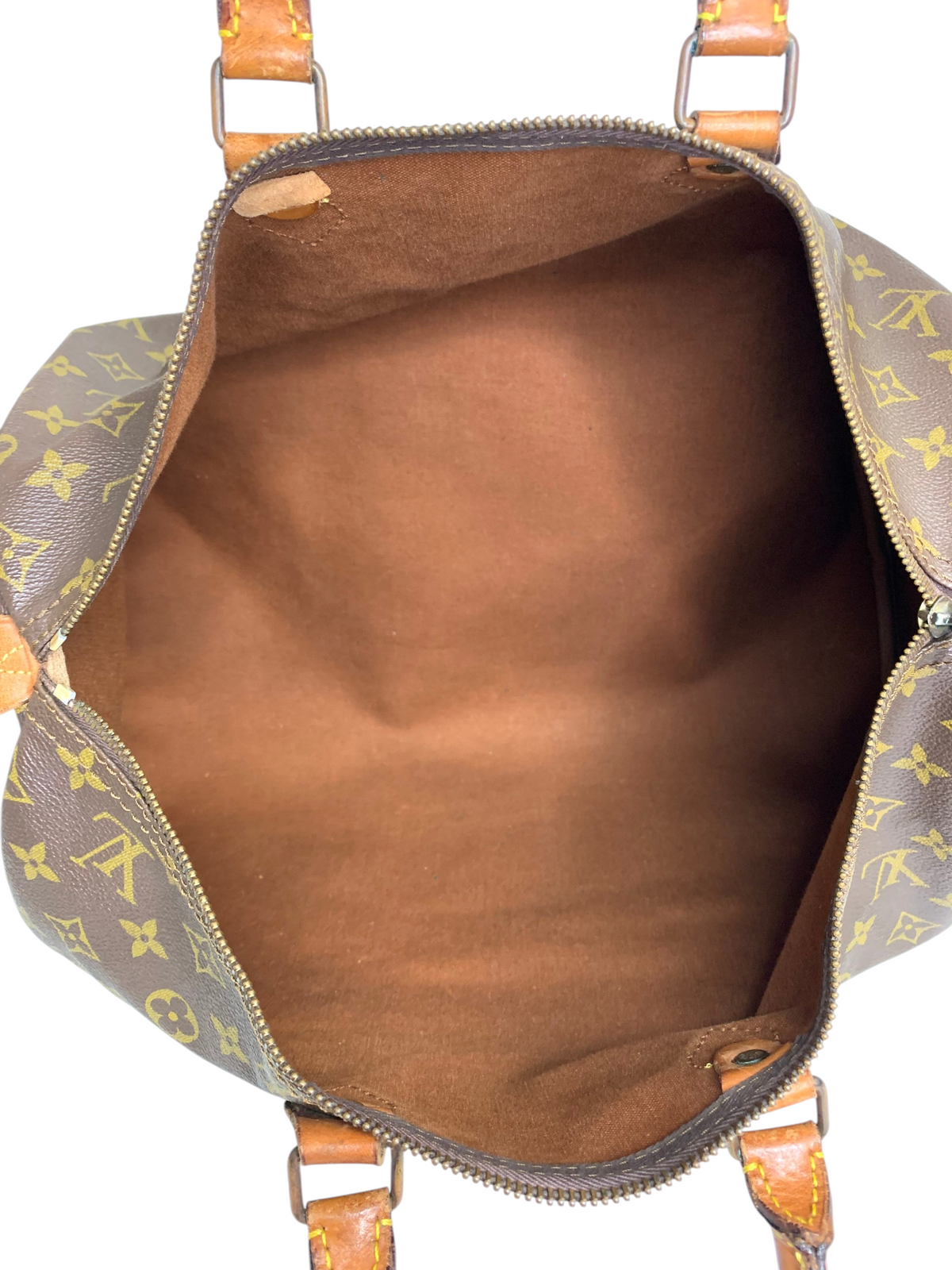 Interior view of a classic monogram coated canvas travel duffel bag with brown fabric lining and leather handles.